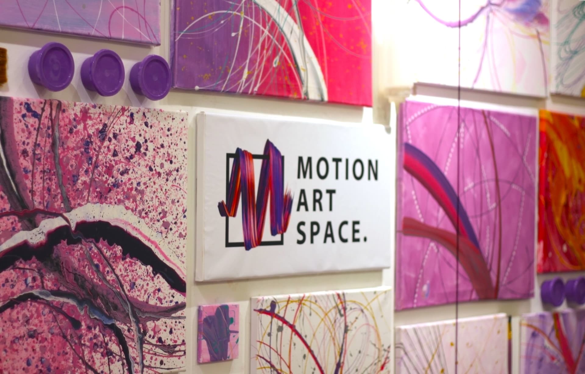A wall of pink and magenta canvases around a Motion Art Space sign, with purple paint cups mounted below.