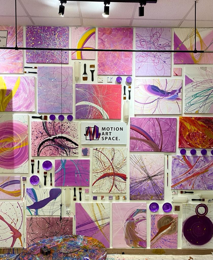 A studio wall tiled with dozens of pink and purple canvases around a Motion Art Space sign.